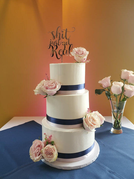 wedding cake topper that says shit just got real on top of white wedding cake in Phoenix.